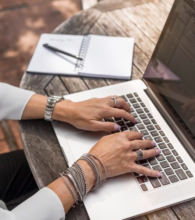 Frauenhände tippen auf einem Laptop, der auf einem braunen Holztisch steht.