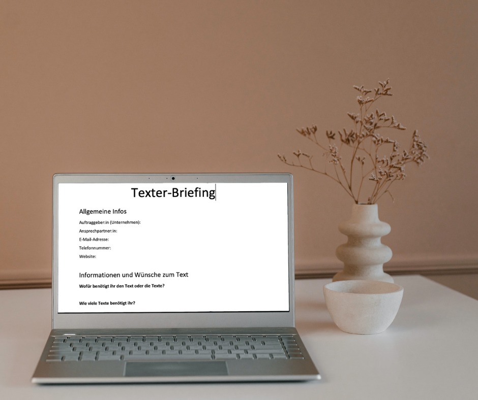 Laptop mit offenem Text-Vorlagen-Dokument "Texter-Briefing" auf einem Tisch, daneben eine leere Schale und eine Vase mit Trockenblumen.